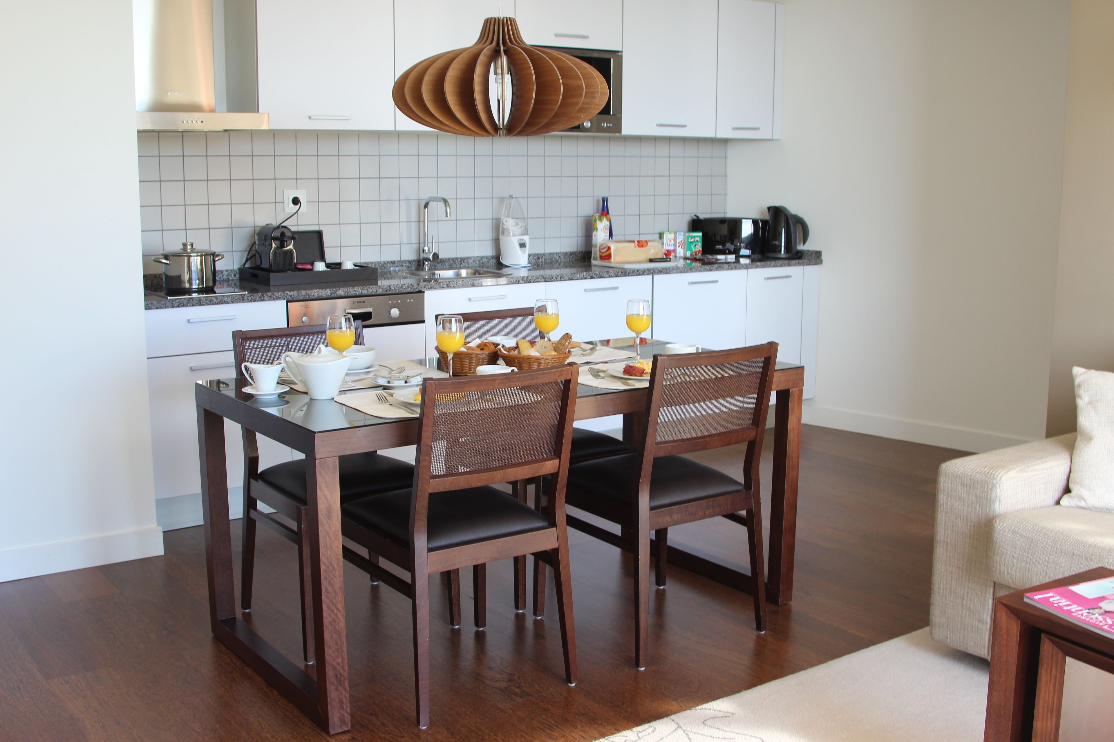 Cozinha moderna com armários brancos, uma mesa de jantar posta para quatro pessoas e uma cafeteira.