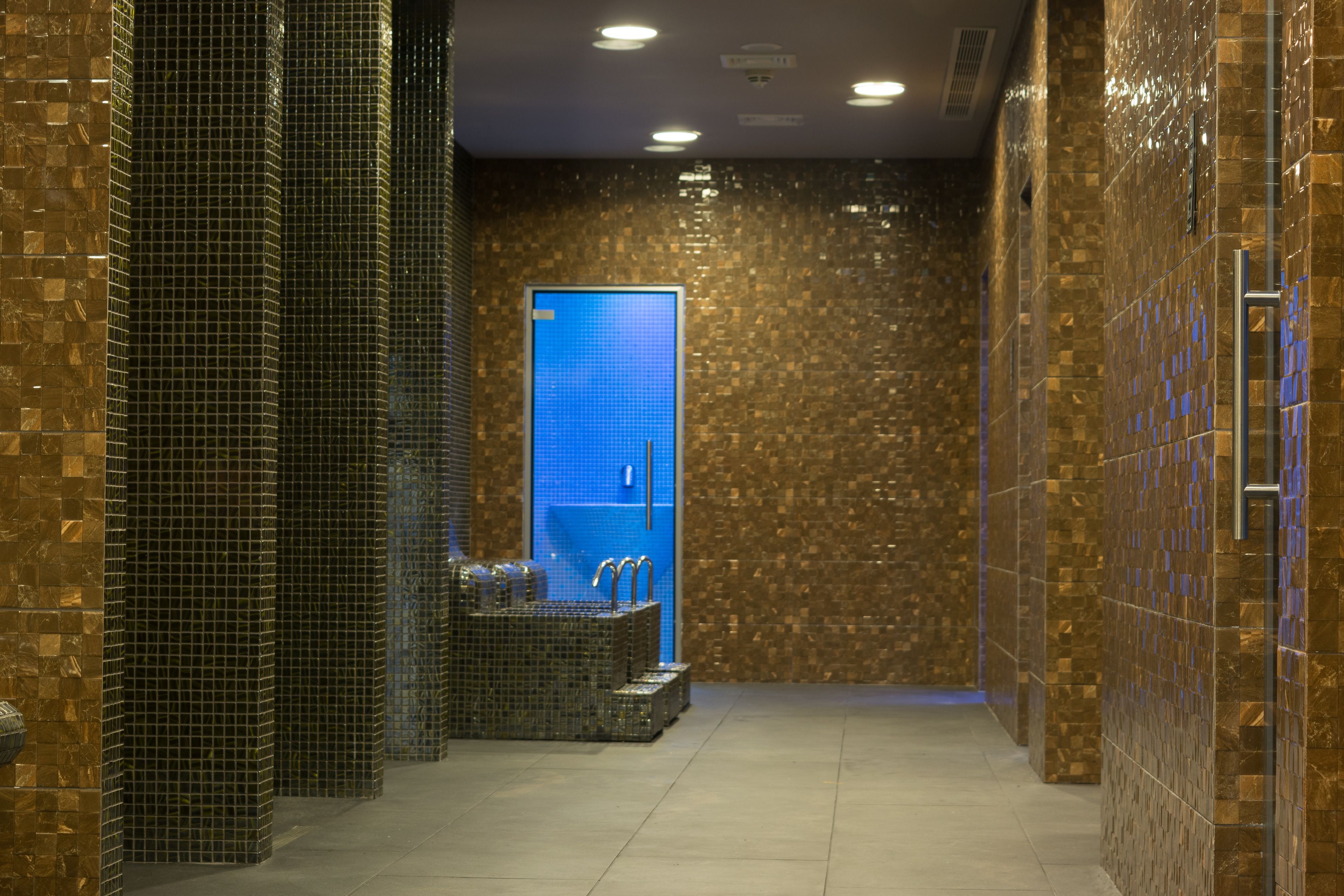 Un baño moderno con paredes de mosaico, un box de ducha con azulejos azules y una pequeña zona de estar con un banco.
