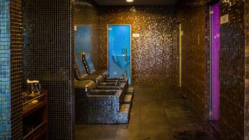 Uma área de spa com uma cadeira de massagem, uma pequena mesa com uma garrafa e um copo, e uma parede revestida com uma porta azul.