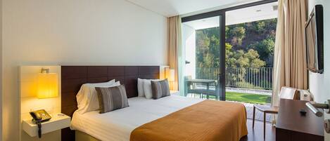 Een hotelkamer met een groot bed, nachtlampjes, een bureau en uitzicht op de omgeving.