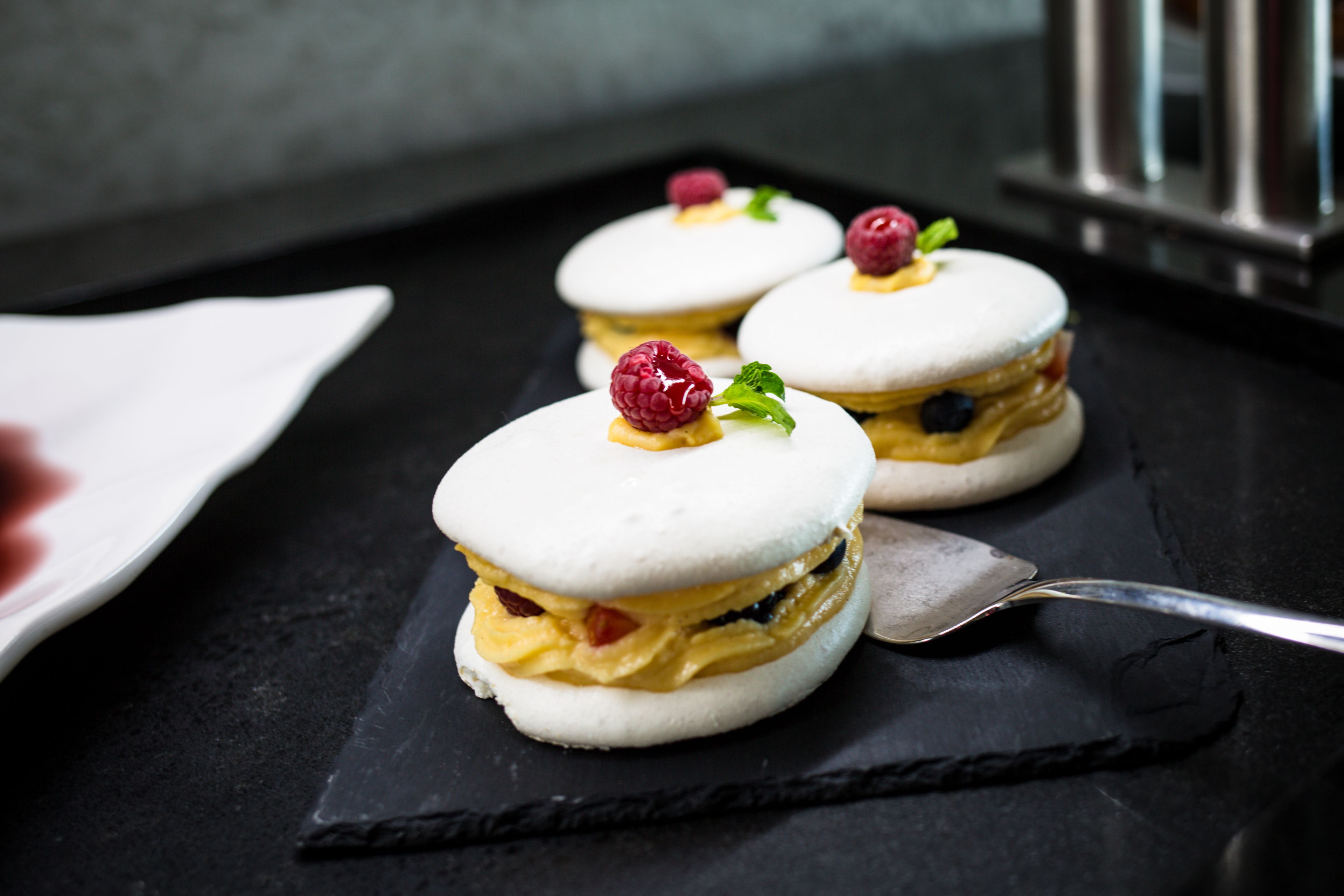 Three dessert sandwiches on a black slate plate with a spoon.