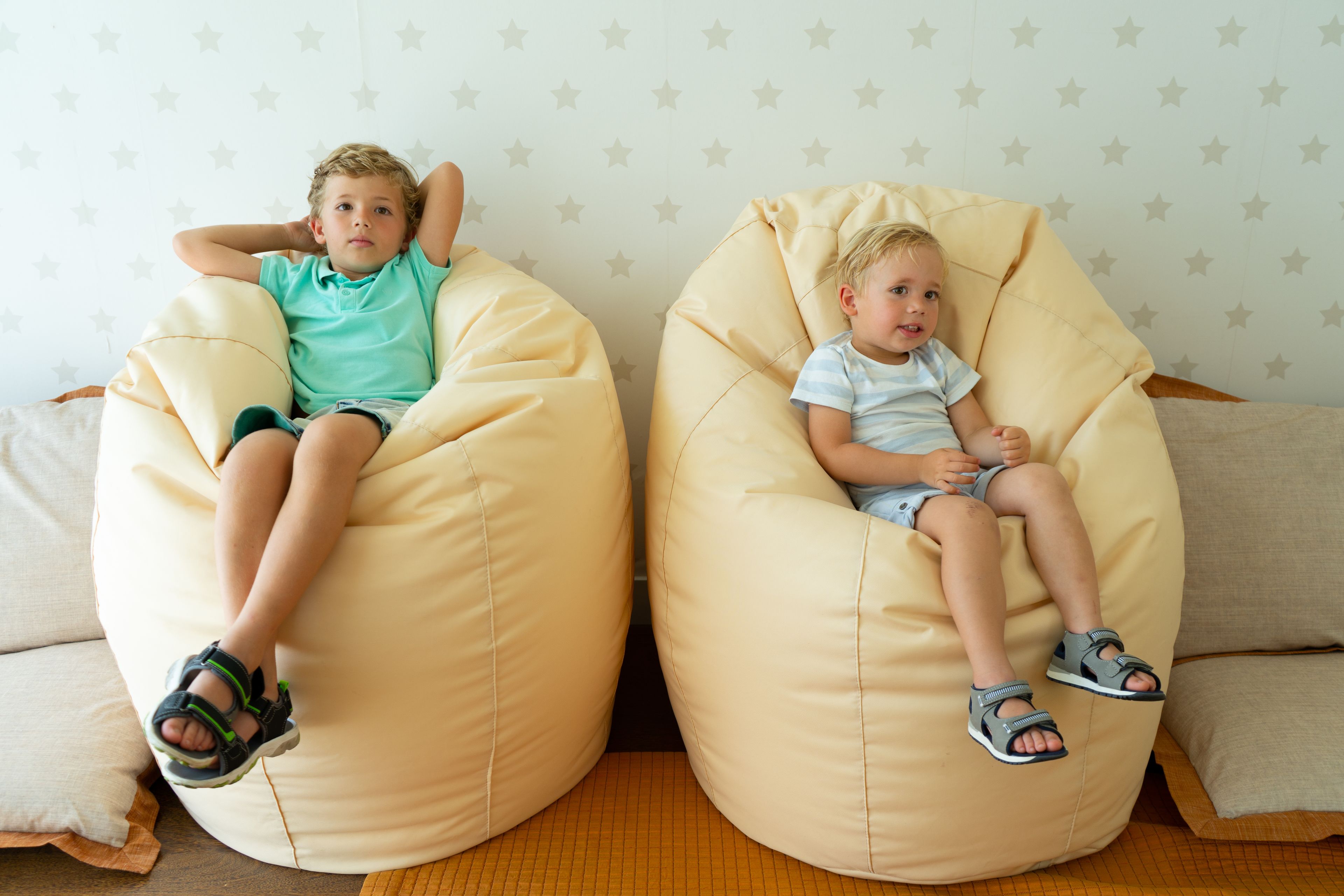 Two children sitting on bean bags in a room with a star-patterned wall.