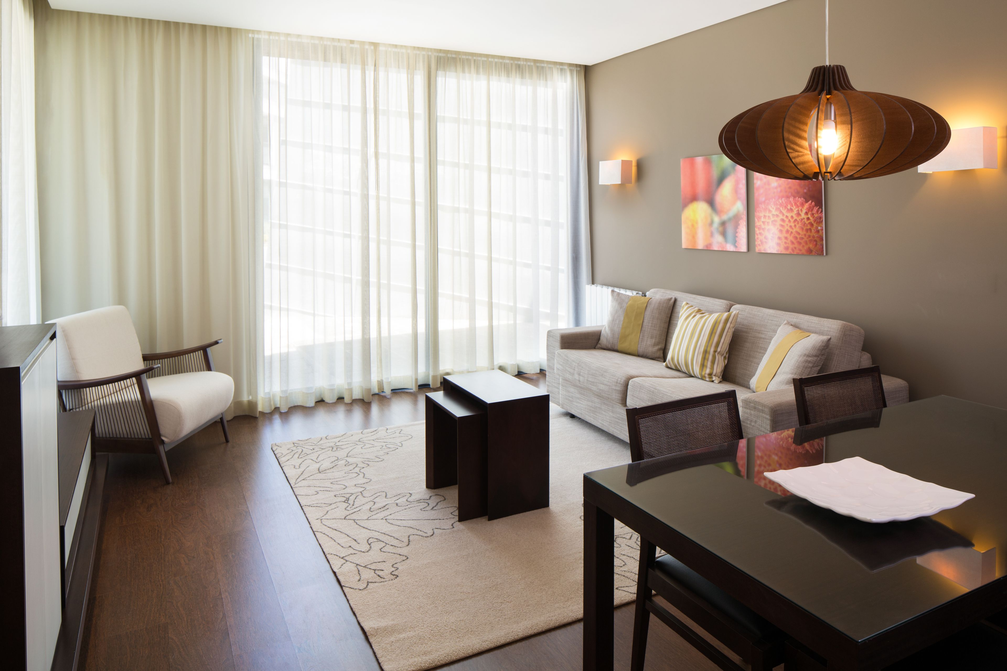 Una sala de estar moderna con sofá, sillones, una mesa de comedor y un ventanal con cortinas translúcidas.