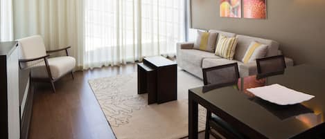 A modern living room with a sofa, armchairs, a dining table, and a large window with sheer curtains.