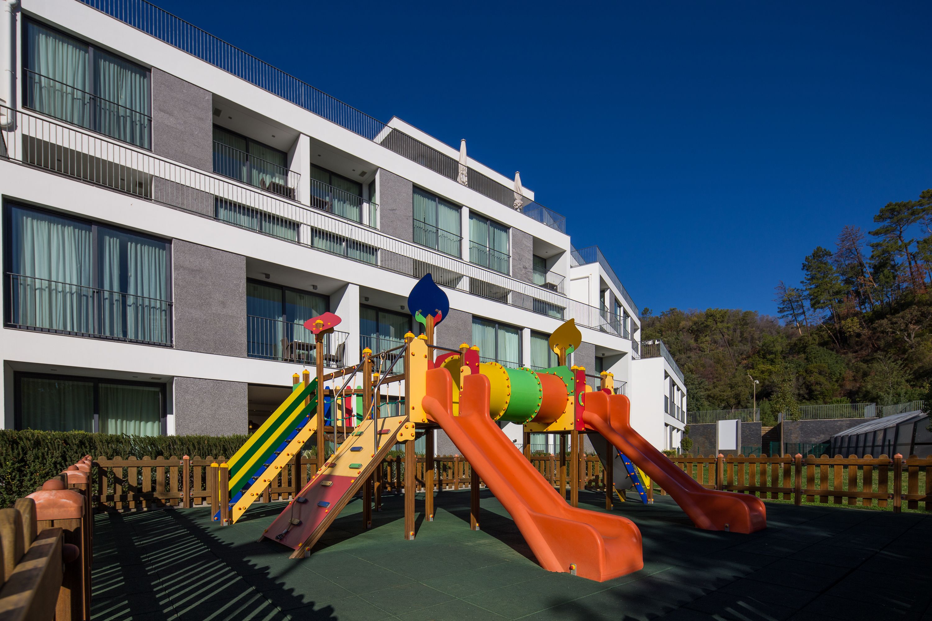 A playground with slides and climbing structures in front of a multi-story building with balconies.