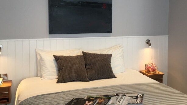 A neatly made bed with white and brown pillows, a magazine on the bed, and a large abstract painting on the wall. - Ilfracombe Carlton Hotel - Hotel (Ilfracombe)