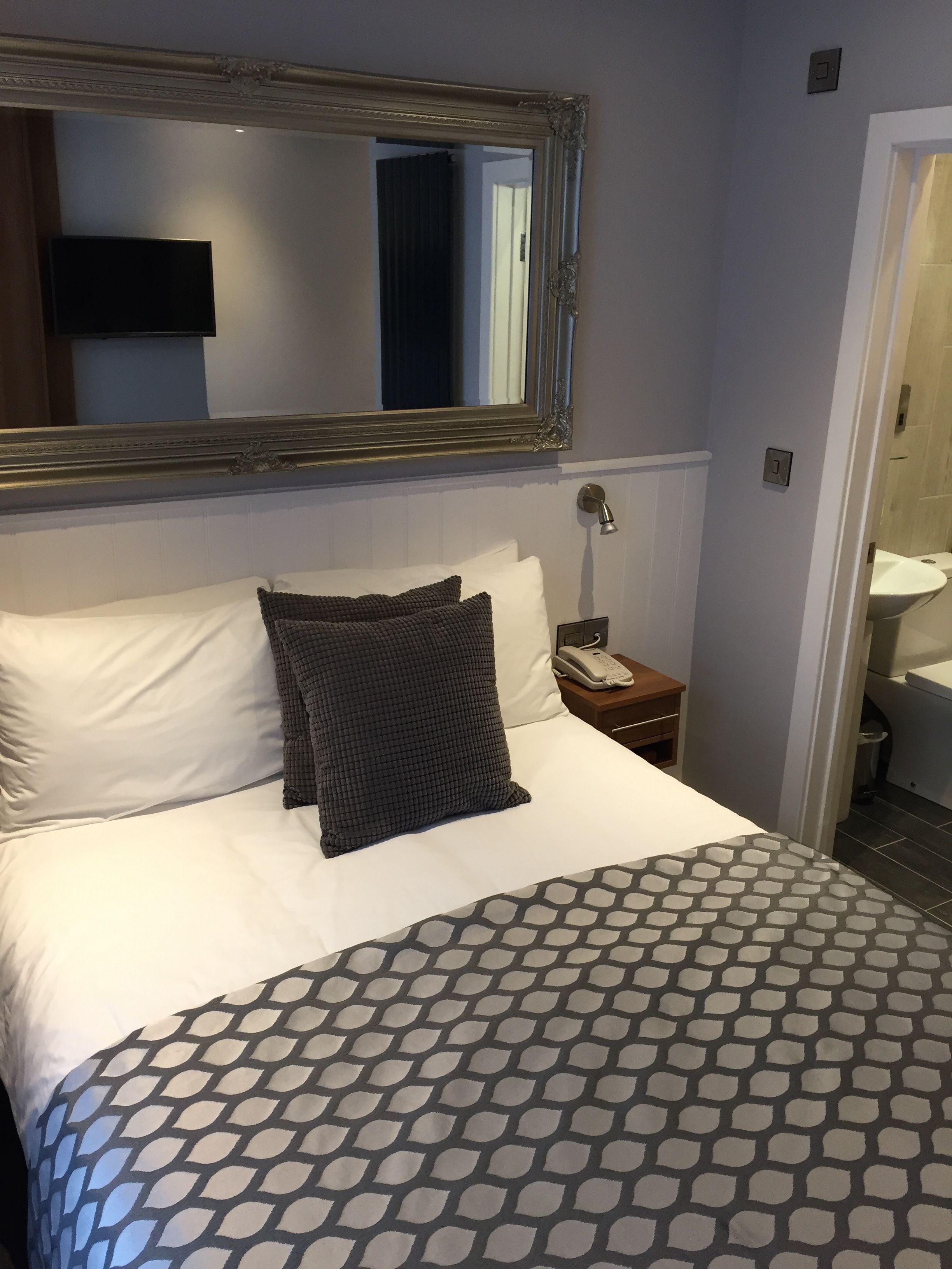 A hotel room with a large bed, a bedside telephone, and a mirror above the bed.