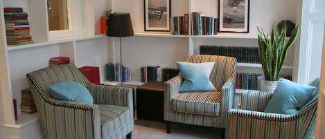 Un salón acogedor con sillones a rayas, una mesa de centro y estanterías llenas de libros.