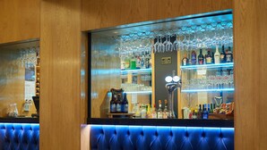 A bar area with a blue cushioned seating area, a well-stocked bar counter with various bottles, and a large window displaying the bar. - Ilfracombe Carlton Hotel - Hotel (Ilfracombe)