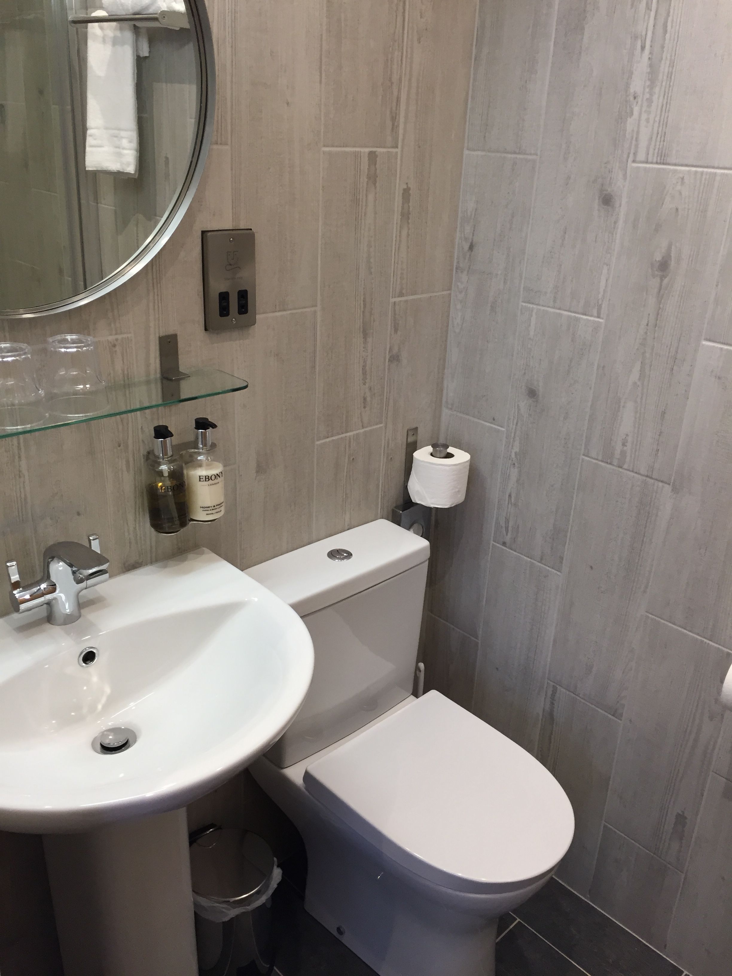 Un baño con un lavabo blanco, un inodoro y un estante de vidrio con artículos de aseo.