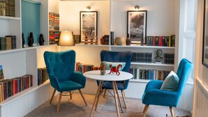 A cozy reading nook with two blue armchairs, a small round table, and a bookshelf filled with books. - Ilfracombe Carlton Hotel - Hotel (Ilfracombe)