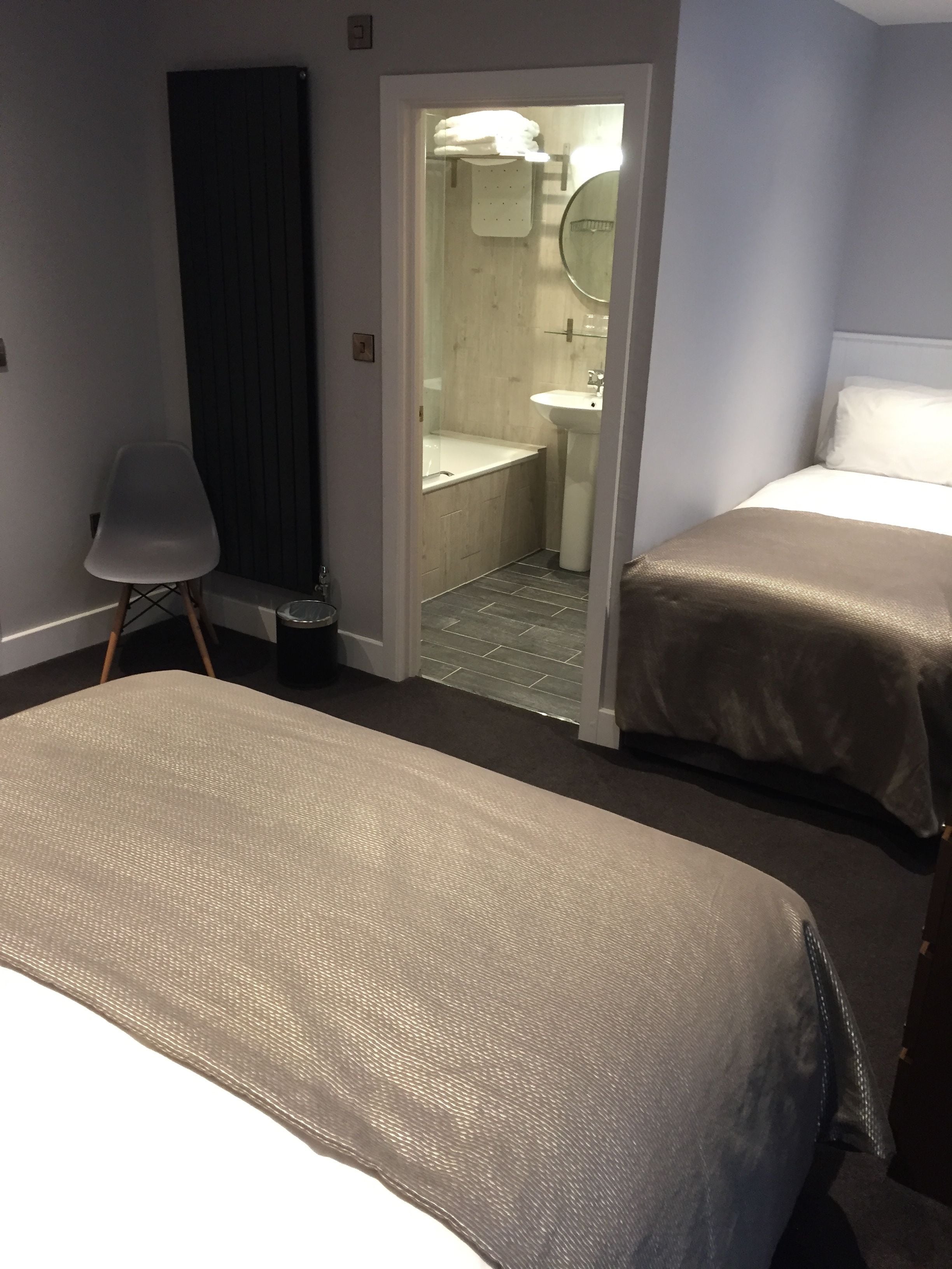 Ein Hotelzimmer mit zwei Betten, einem Sessel, einem kleinen Tisch und einem durchgegangenen Tür angedeuteten Badezimmer.