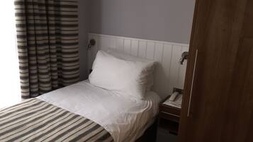 A hotel room with a bed, a bedside table with a phone, and a striped curtain.