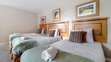 Habitació d'hotel amb tres llits individuals, cadascun amb una manta verda i una tovallola blanca. Hi ha tres quadres emmarcats penjats a la paret sobre els llits.