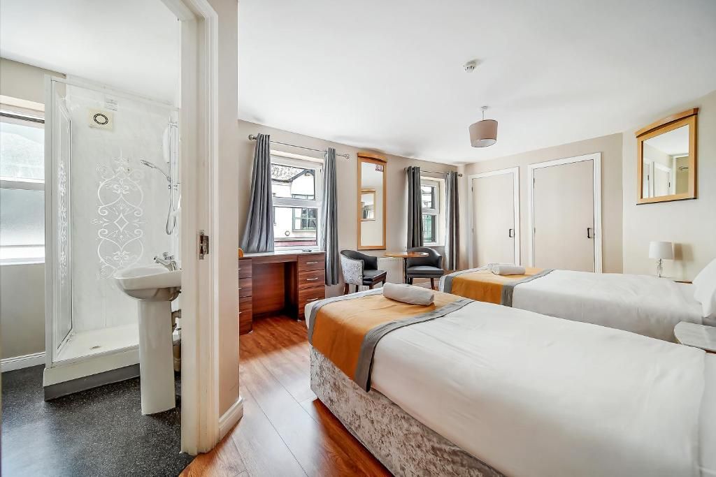 Habitación de hotel con ducha, escritorio, dos camas, zona de estar y baño.