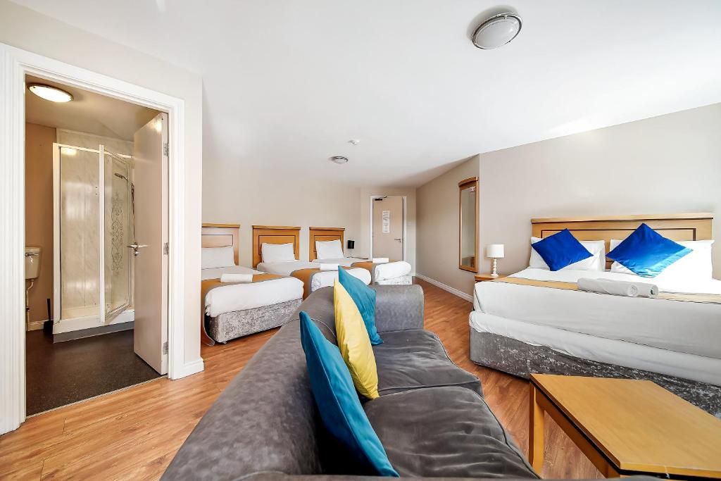A hotel room with a sofa, two beds, a wooden floor, and a bathroom with a glass shower.