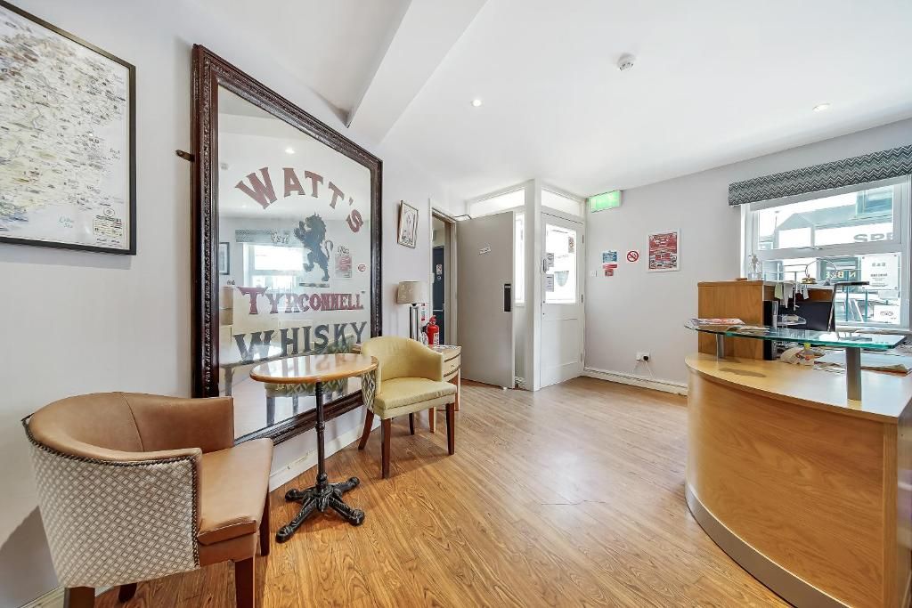 A reception area with a wooden reception desk, a framed whiskey advertisement, a patterned armchair, and a small round table.