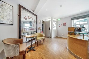 Un área de recepción con un mostrador de madera, un anuncio enmarcado de whisky, un sillón estampado y una pequeña mesa redonda.