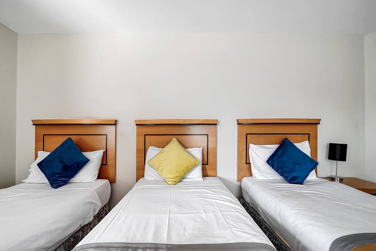 A hotel room with three single beds, each with a wooden headboard and white bedding.