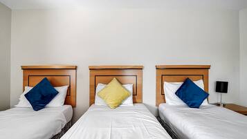A hotel room with three single beds, each with a wooden headboard and white bedding.