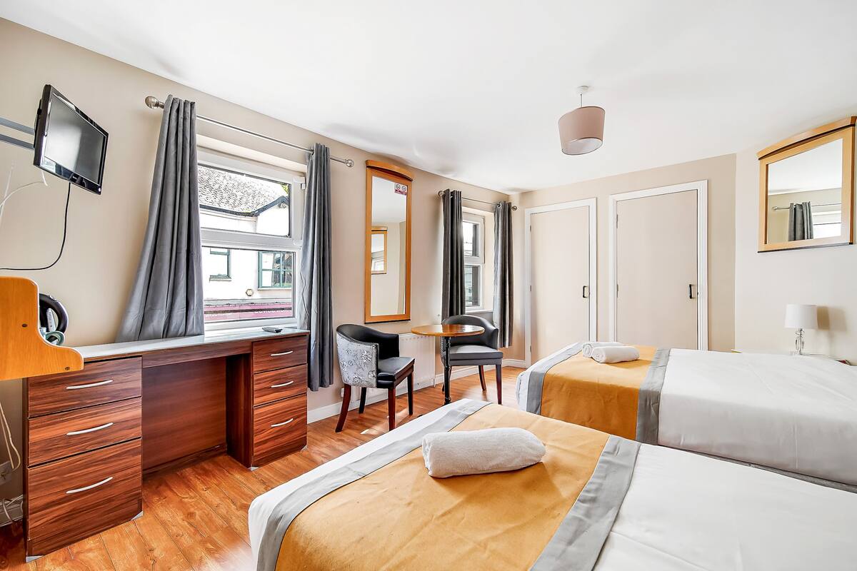 A hotel room with two beds, a desk, a chair, a TV, and a window with curtains.