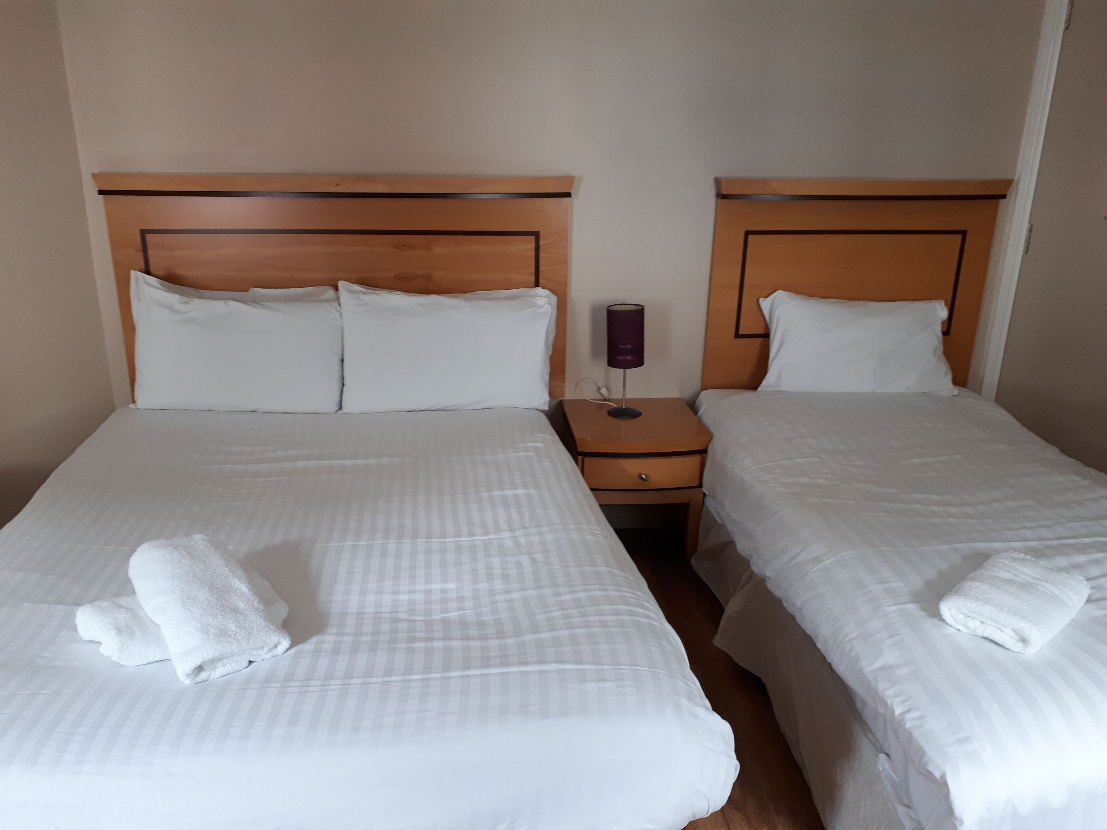 Una habitació d'hotel amb dos llits individuals, cadascun amb un panell de fusta al capçal, roba de llit blanca i una taula de nit amb una làmpada.