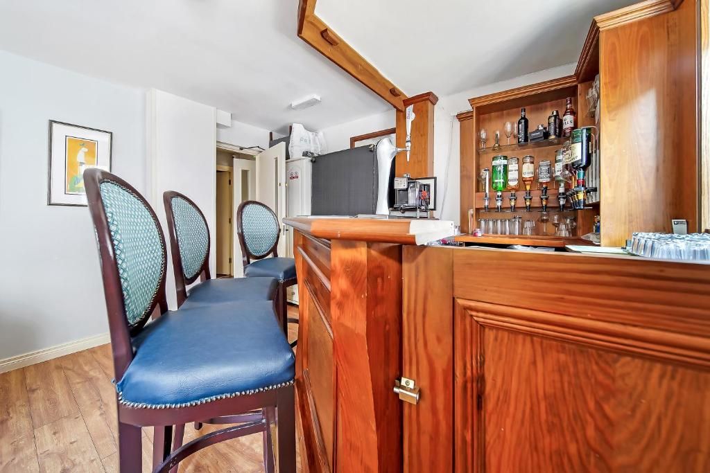 A bar area with a wooden counter, bar stools, and a shelf with various bottles.