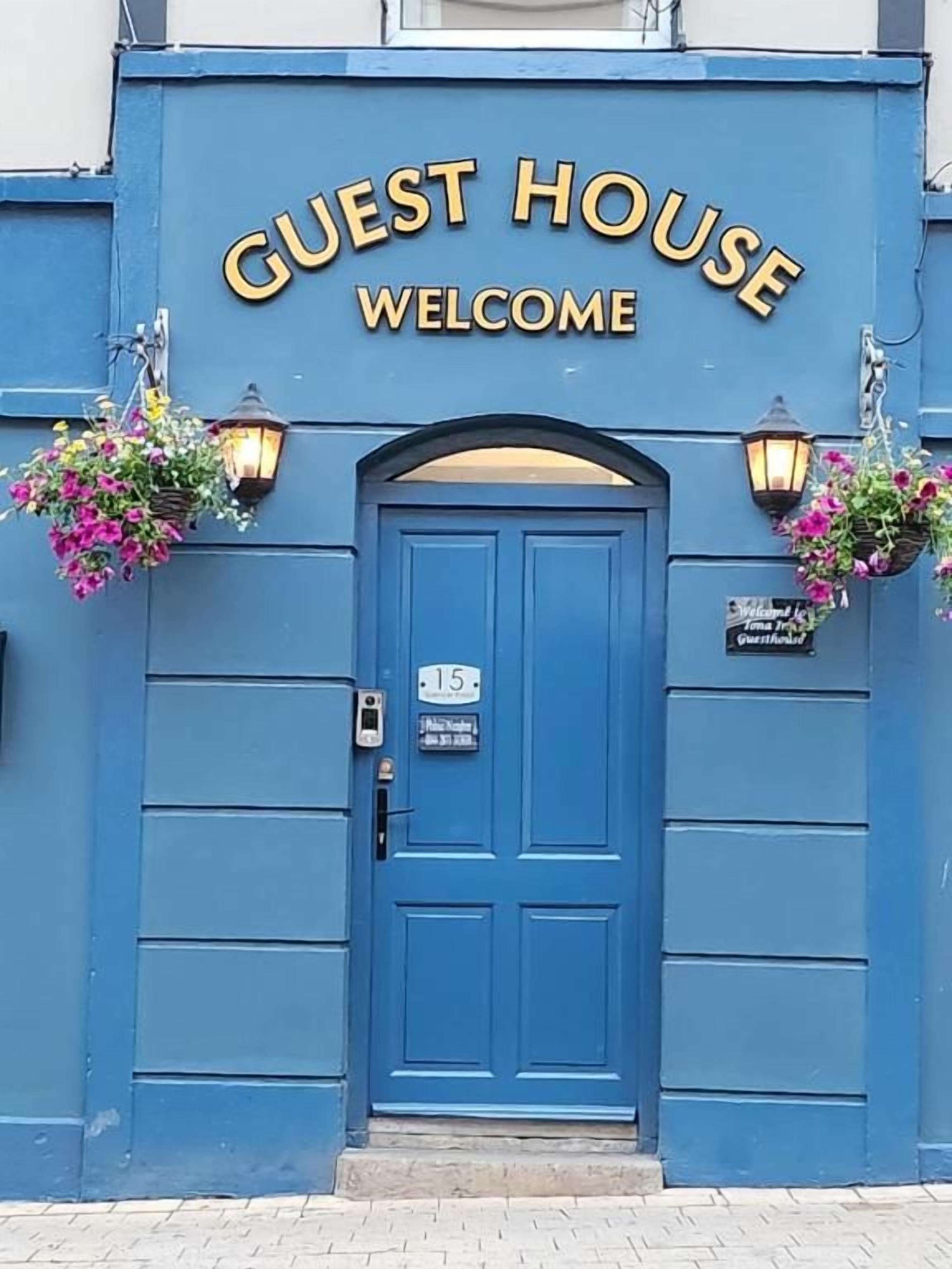 A blue building with a sign that reads 'GUEST HOUSE WELCOME' above a door marked with the number 15.