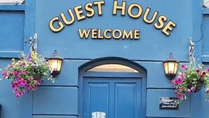 A blue building with a sign that reads 'GUEST HOUSE WELCOME' above a door marked with the number 15.