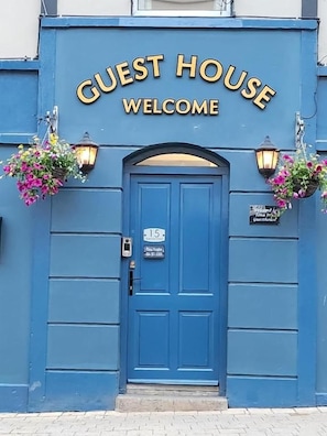 Edifici blau amb un rètol que diu 'GUEST HOUSE WELCOME' sobre una porta amb el número 15.
