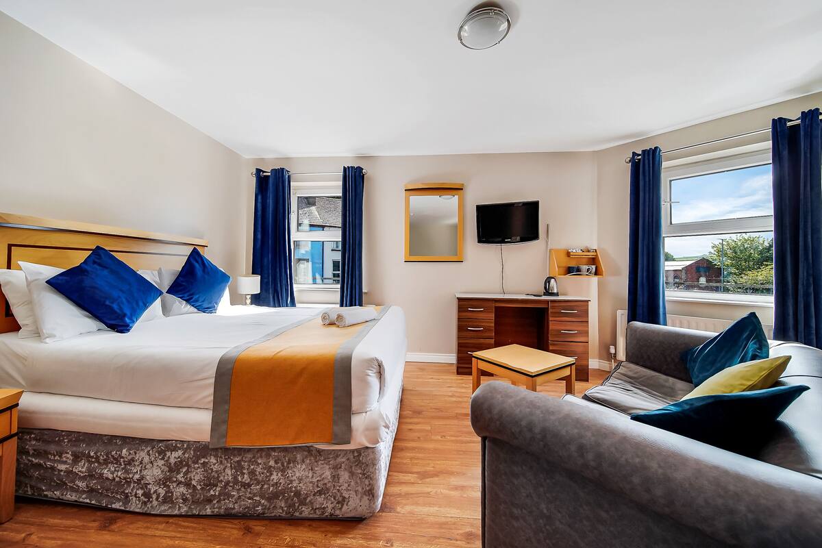 A hotel room with a bed, a desk, a chair, a TV, and a window with curtains.
