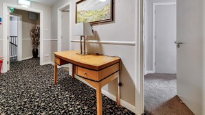 A hallway with a wooden desk, a framed painting, and a carpeted floor.