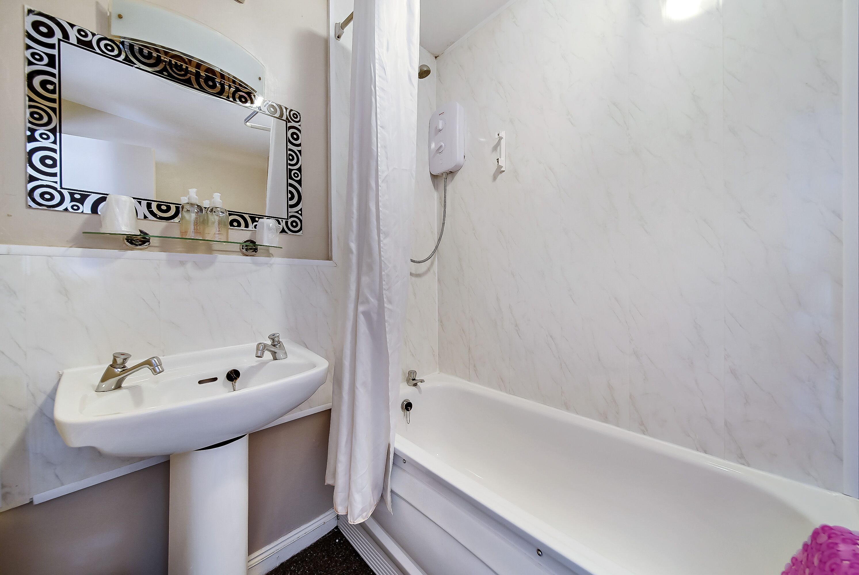 Un bany amb un lavabo blanc, un mirall amb marc decoratiu i una banyera.