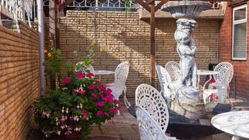 A patio with white metal chairs and tables, a stone fountain, and a brick wall.