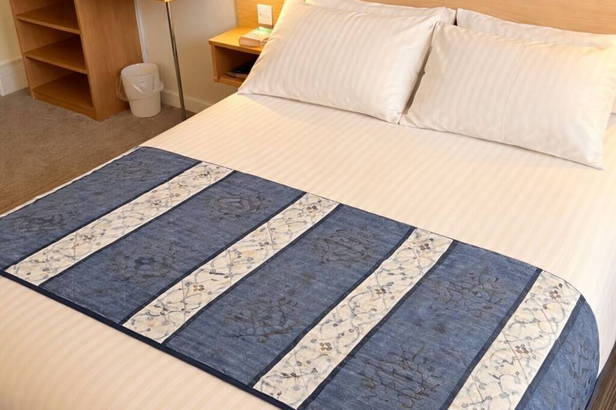 A hotel room with a bed, a bedside table with a lamp, a nightstand, and a mirror.