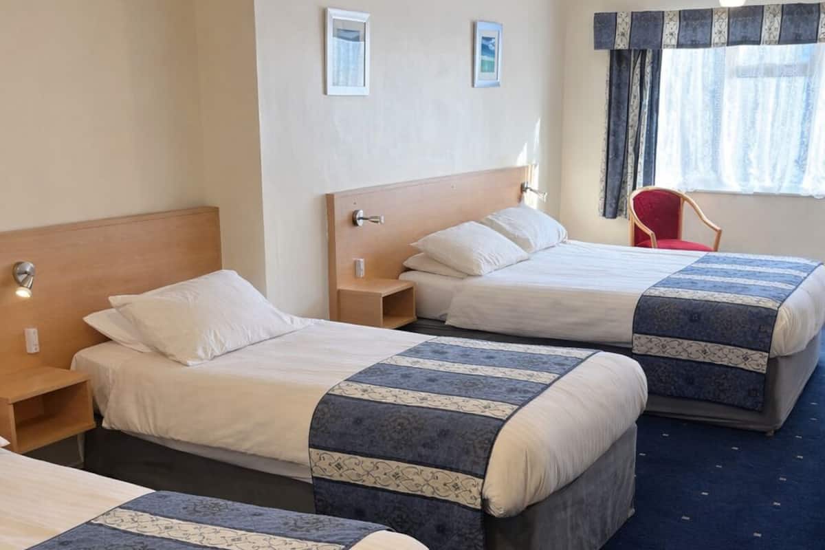 A hotel room with three beds, a red chair, and a large window with curtains.