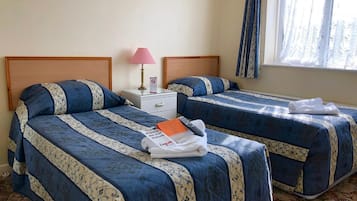 A hotel room with two beds, a nightstand, a lamp, and a window with curtains.