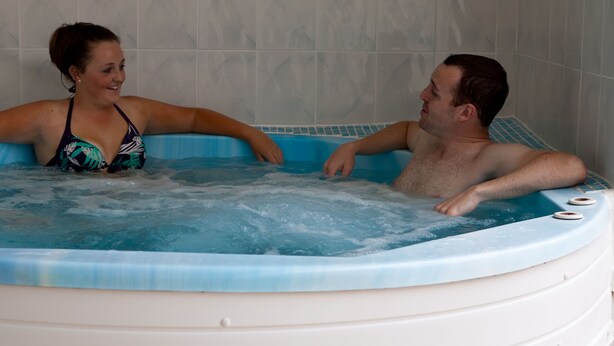 Um casal em uma banheira de hidromassagem com um fundo de parede azulejada.