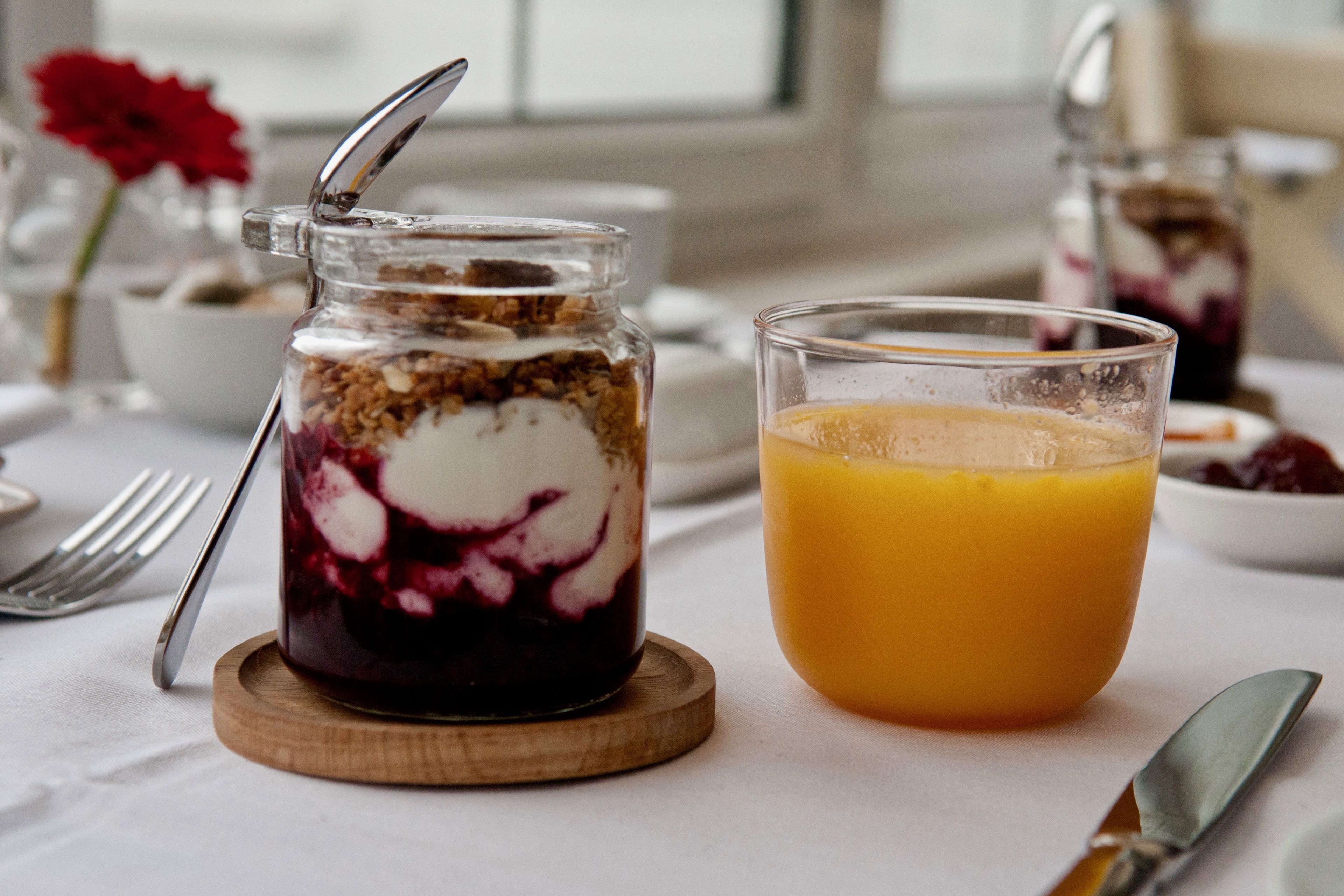 A breakfast setting with a glass of orange juice and a layered dessert in a jar.