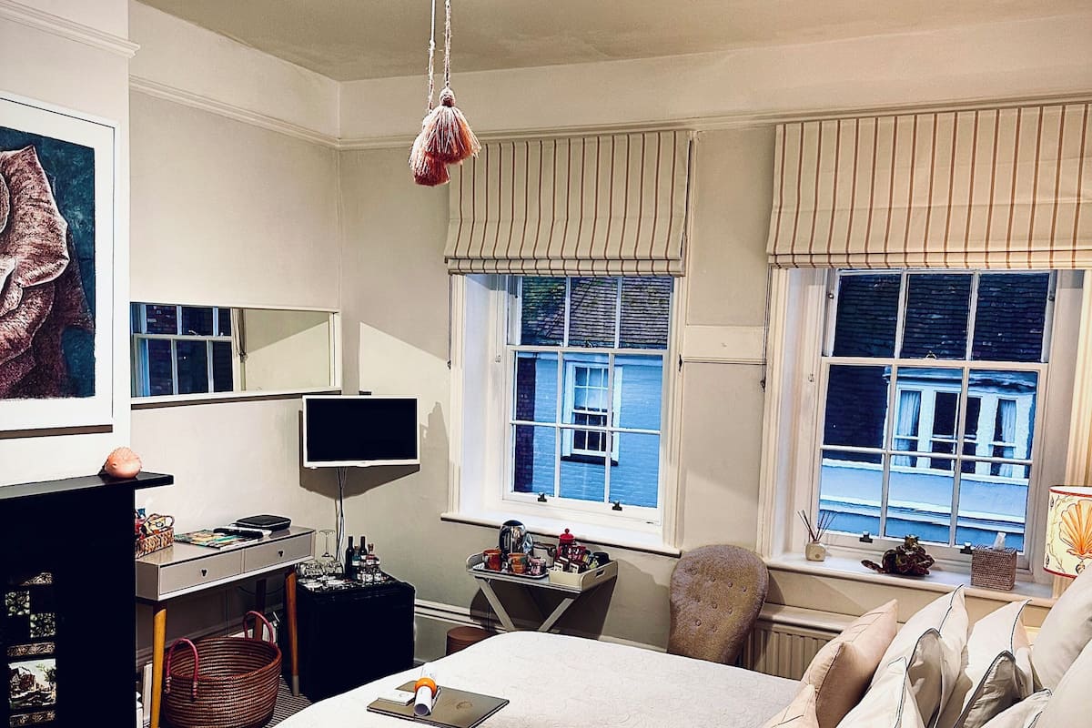 Habitación de hotel con cama, escritorio, silla, televisor y ventana con vista a edificios.