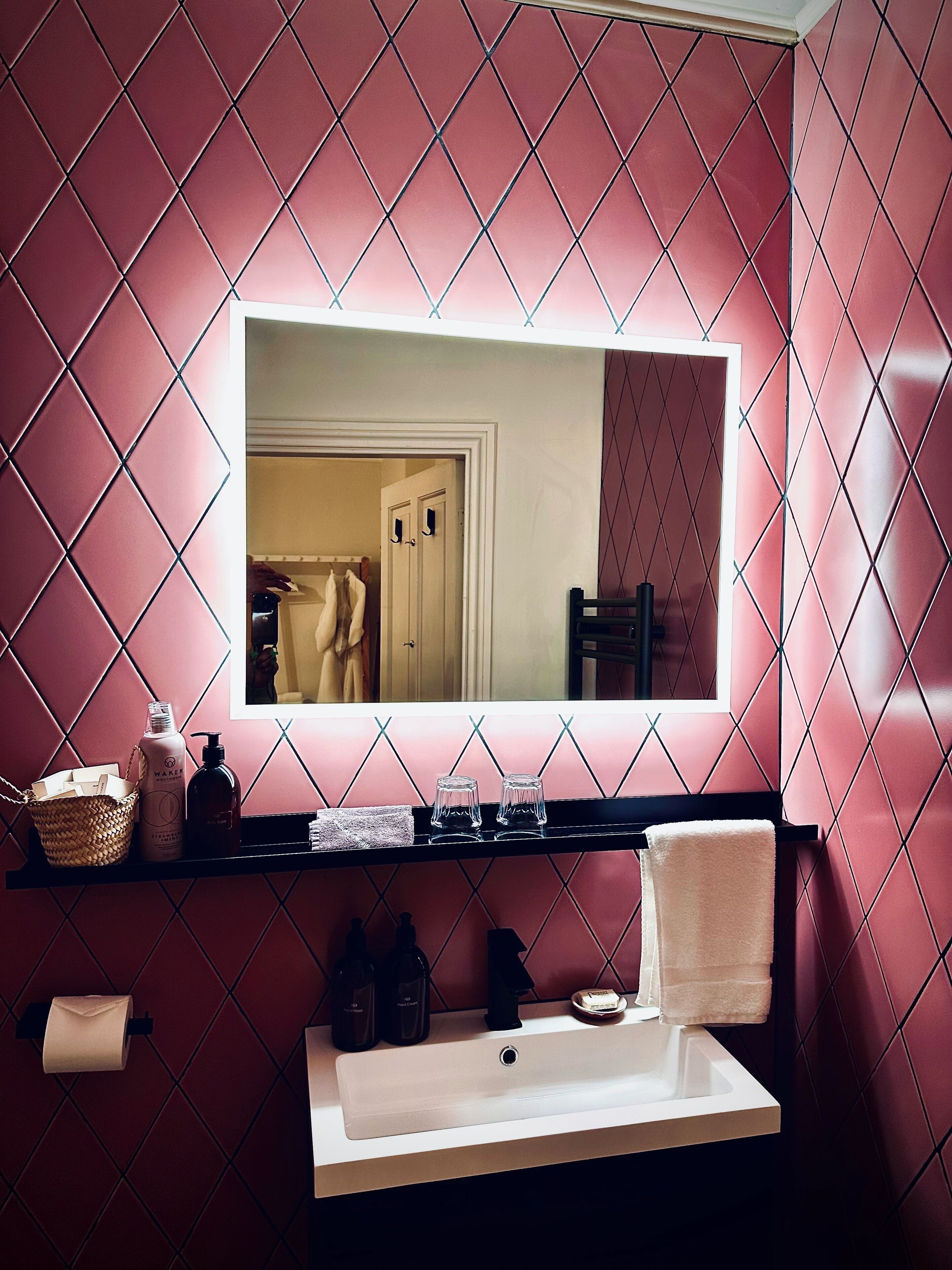 A bathroom with a large mirror, a sink, and a shelf with toiletries.