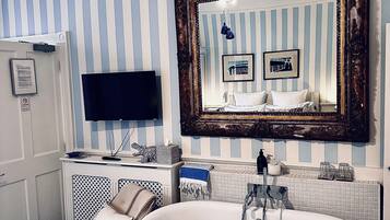 A bathroom with a freestanding bathtub, a large mirror, and a television on a cabinet.
