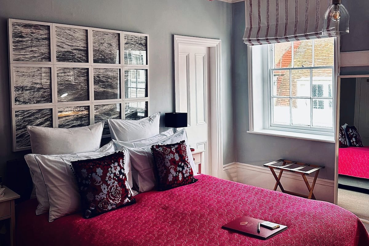 Un dormitorio con una cama grande, un ventilador de techo, una ventana con cortinas y una obra de arte en la pared.