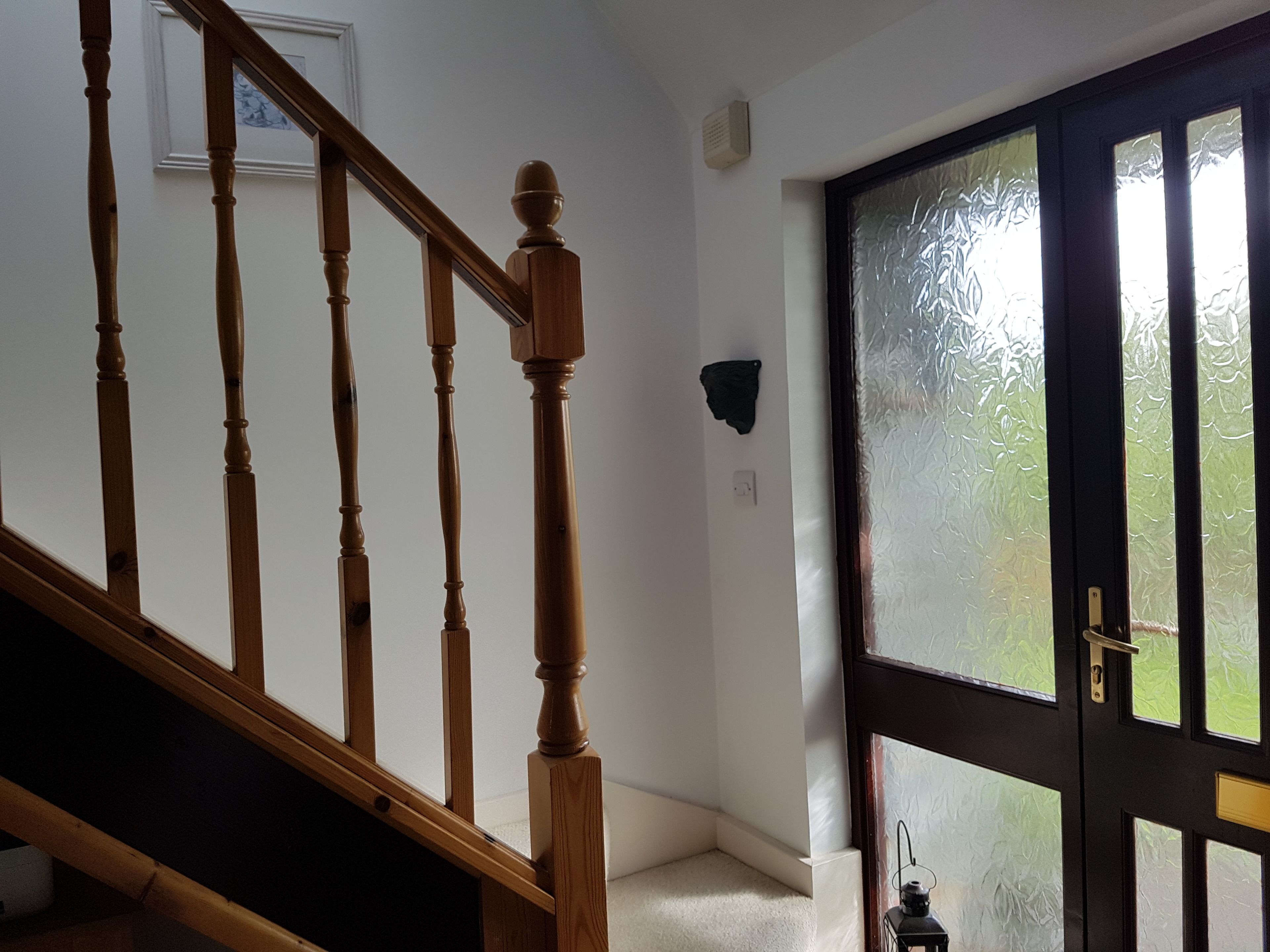 Una escalera de madera que conduce a una habitación con una puerta de vidrio satinado y un pequeño farol en el suelo.