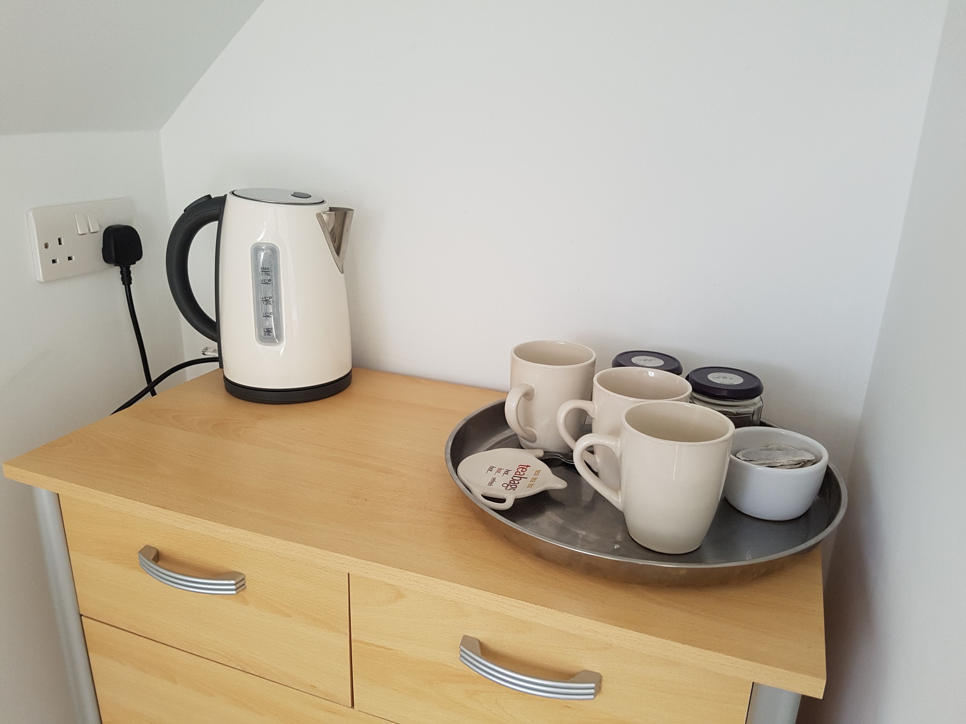 Une petite cuisine équipée d’une bouilloire blanche, de plusieurs tasses et d’un plateau contenant des sachets de thé.