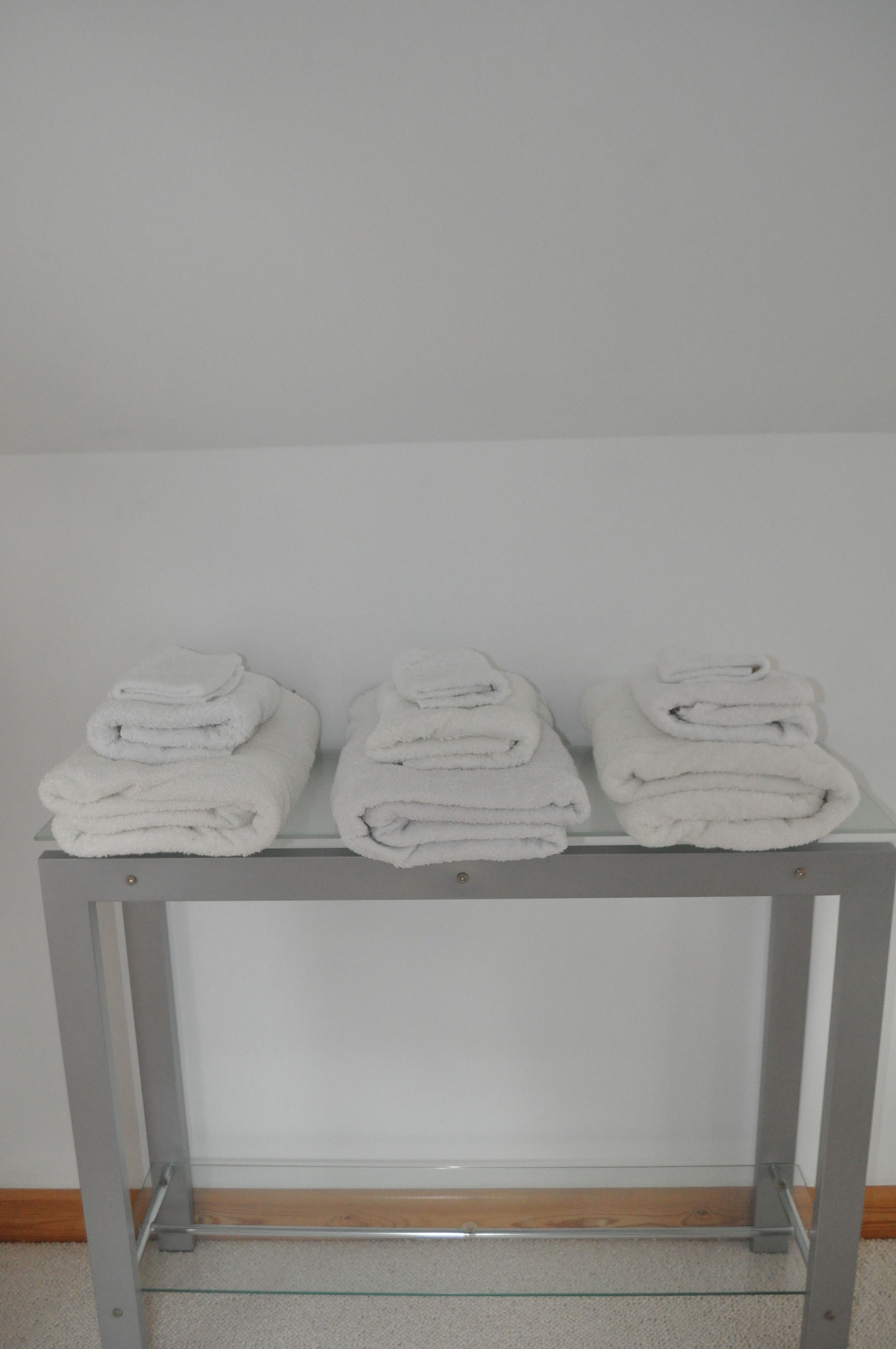 A glass-top table with three neatly folded white towels stacked on it.