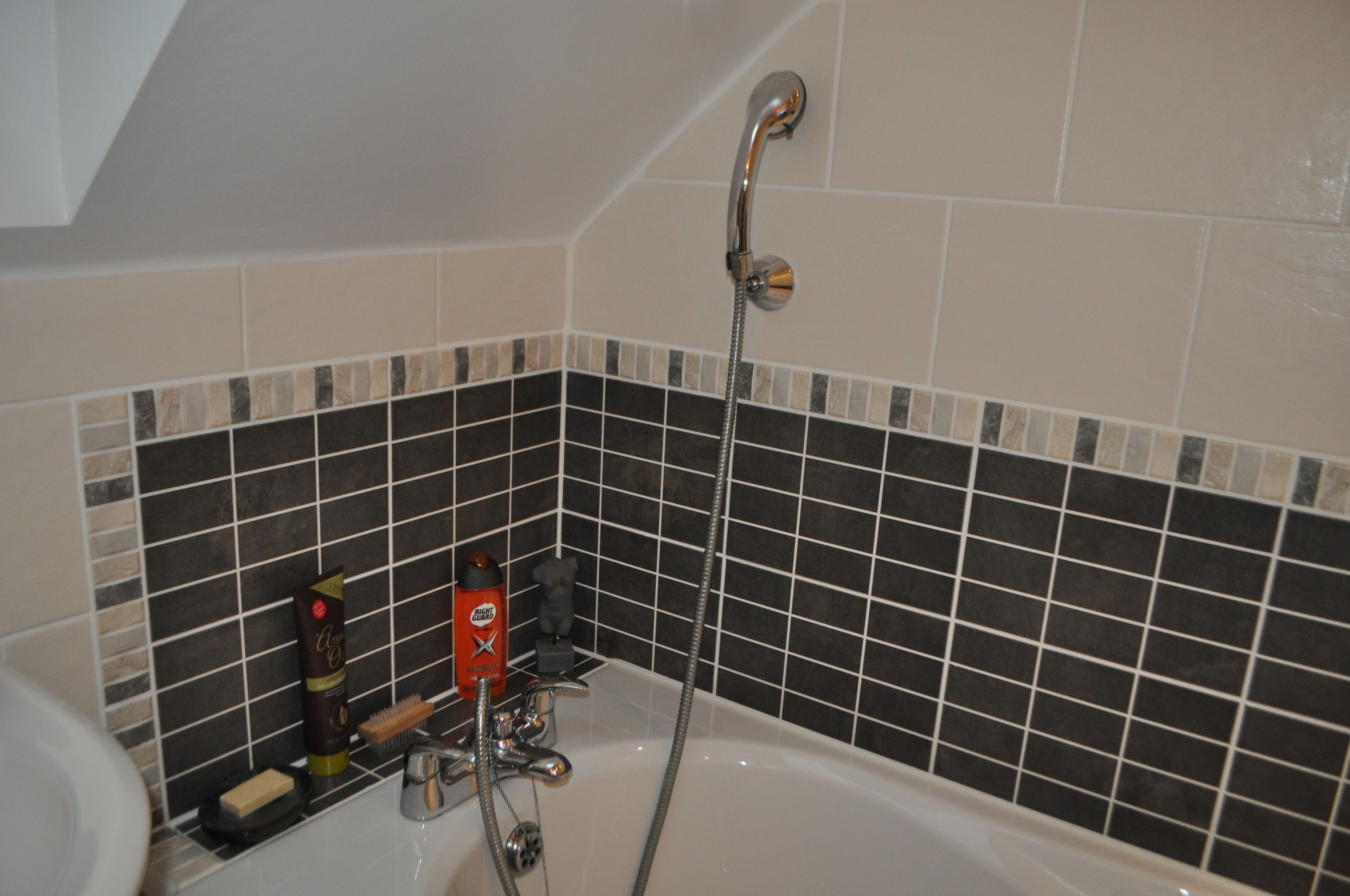 Een badkamer met een bad, douche en betegelde wand.