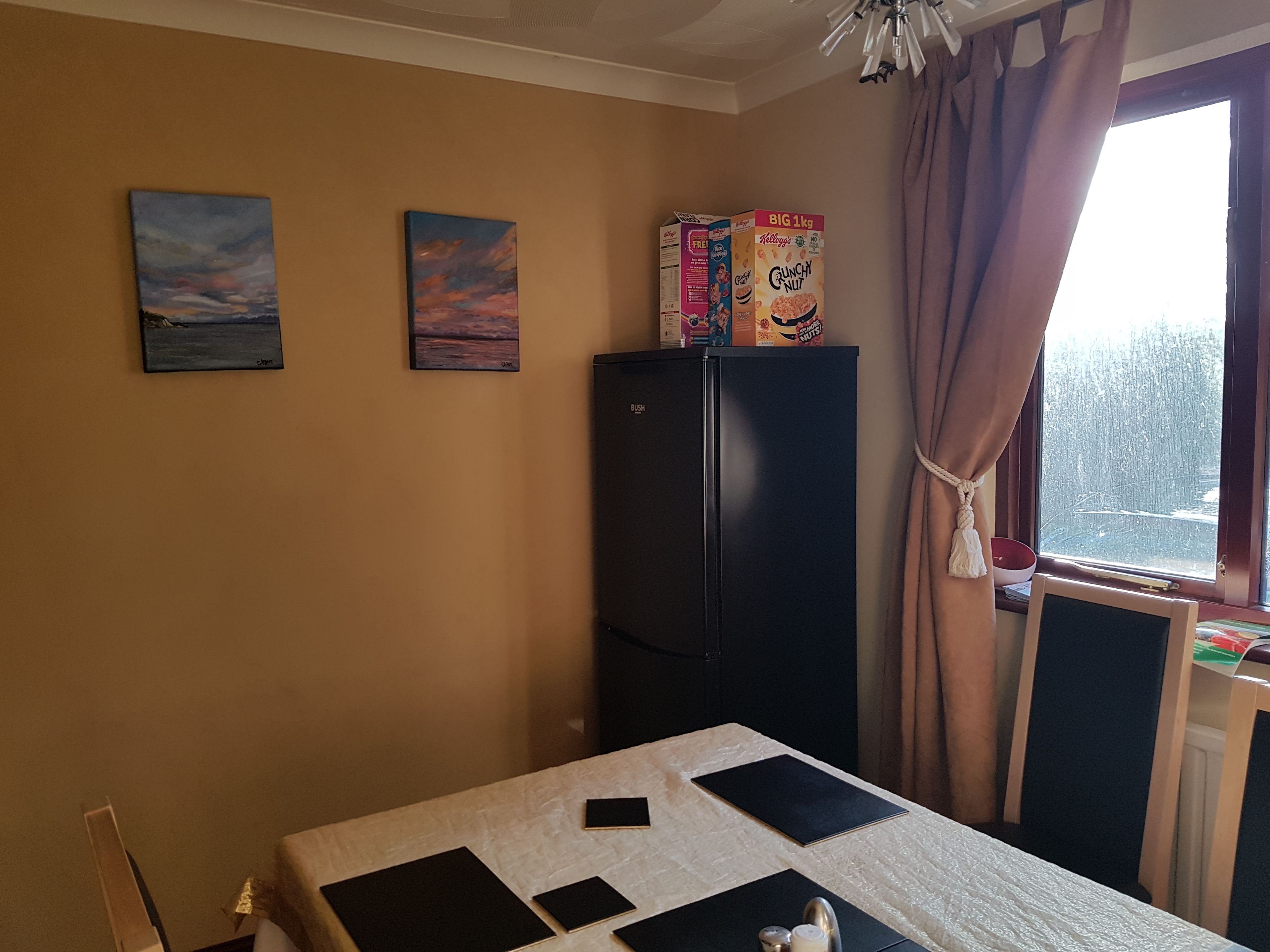 A room with a bed, a black refrigerator, and two paintings on the wall.