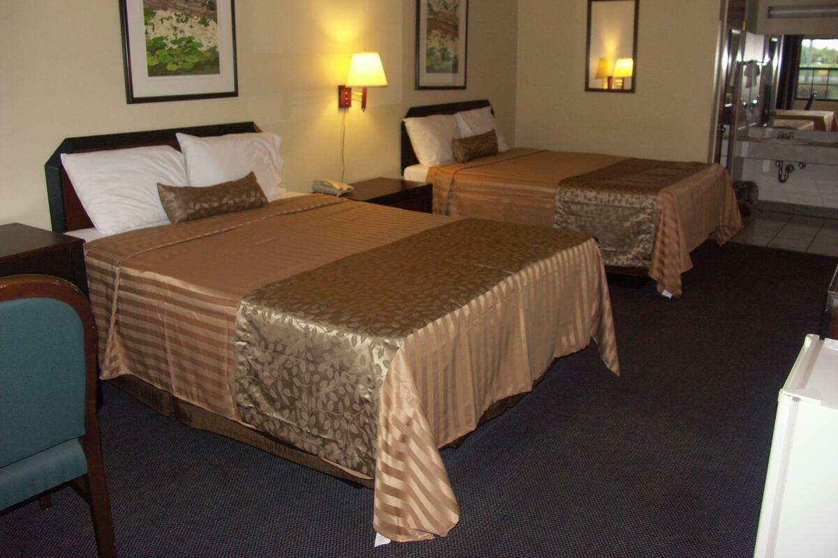 A hotel room with two beds, a desk, a chair, and a bathroom.