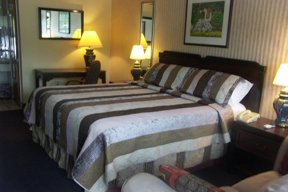 A hotel room with a large bed, two bedside tables, a chair, and a desk with a lamp.